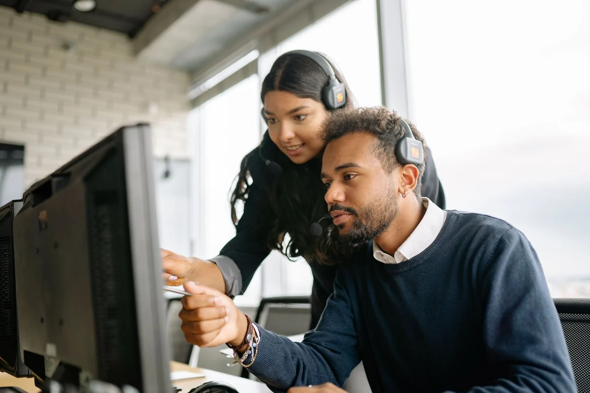 Zwei Mitarbeitende mit Headsets besprechen etwas am Bildschirm