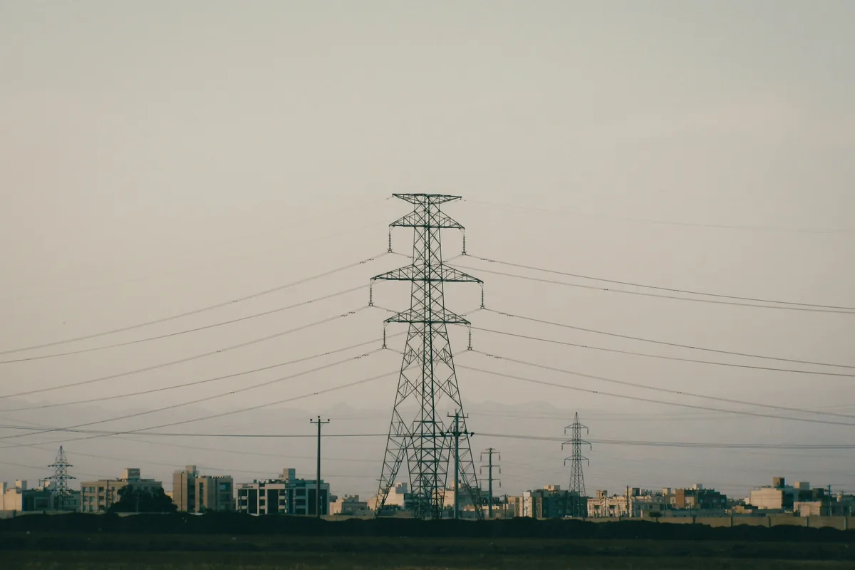 Strommast mit Freileitungen über den Dächern einer Stadt