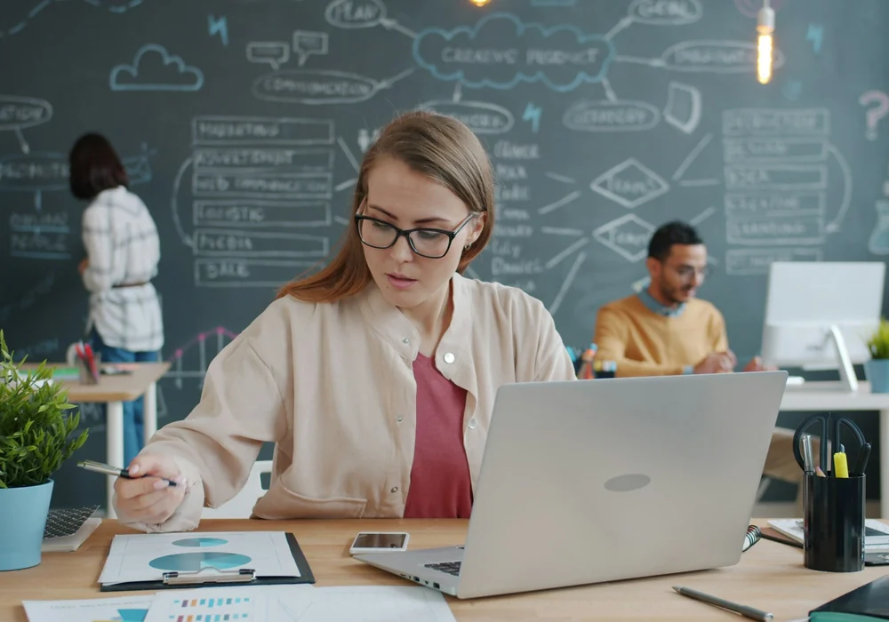 Frau am Laptop wertet ausgedruckte Diagramme aus