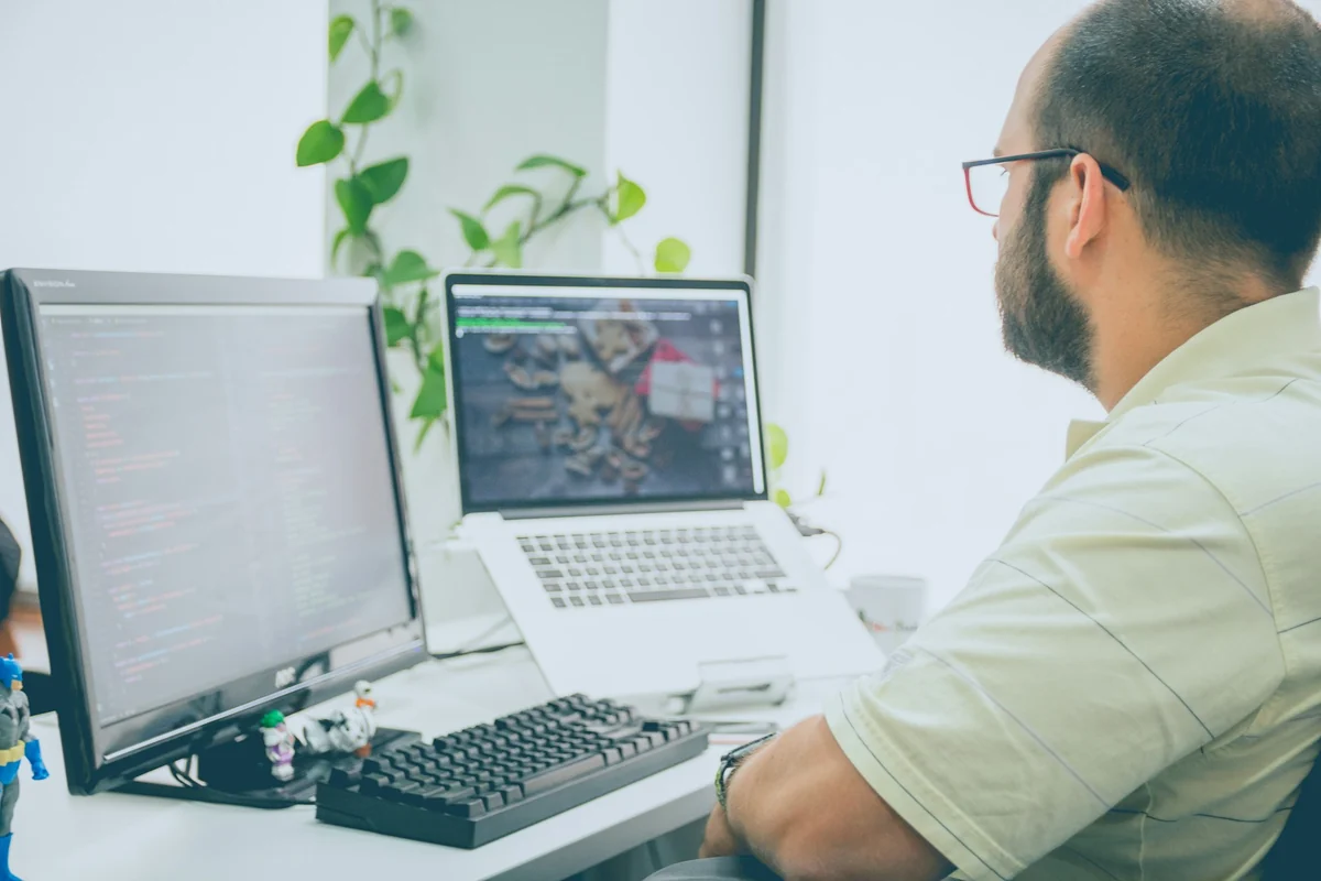 Arbeitsplatz mit mehreren Bildschirmen und Notebook, auf einem Monitor läuft Programmcode