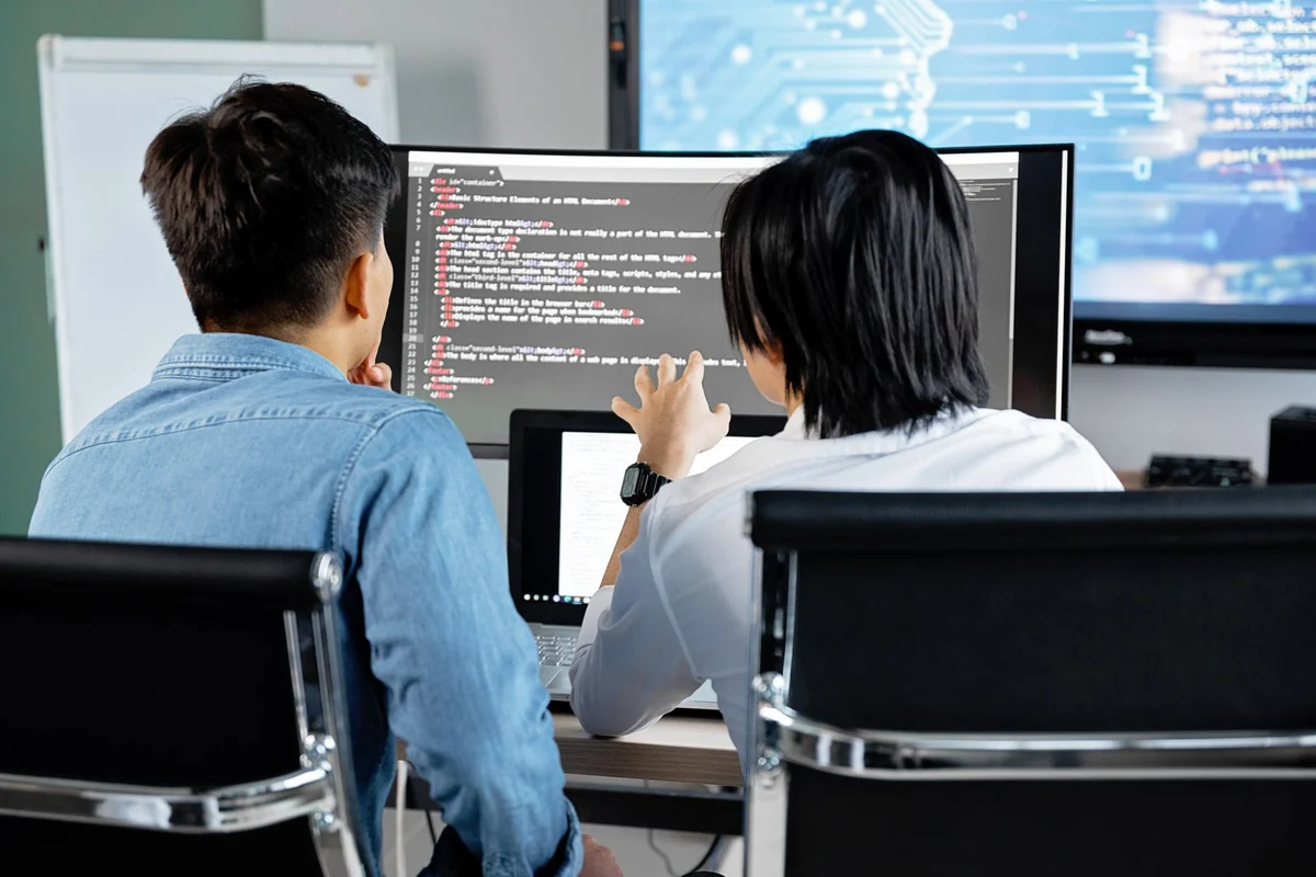 Zwei Entwickler an nebeneinanderstehenden Monitoren mit Quellcode