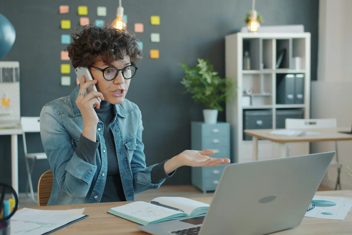 Mitarbeiterin telefoniert am Schreibtisch neben ihrem Laptop